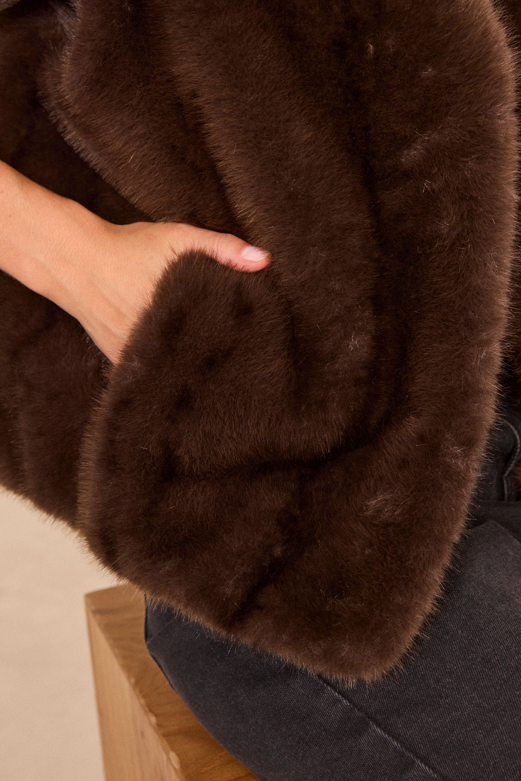Détail d'une veste en fausse fourrure marron foncé, main dans la poche